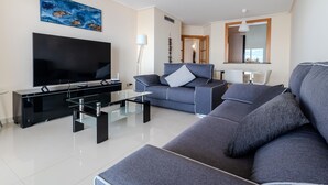 A modern living room with a flat-screen TV, a sofa, a glass coffee table, and a painting on the wall. - 3-Bedroom Apartment in Roses with Wi-Fi and Parking (Roses)
