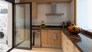 A modern kitchen with a dishwasher, a built-in oven, wooden cabinets, and a large window. - 3-Bedroom Apartment in Roses with Wi-Fi and Parking (Roses)