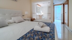 A hotel room with a large bed, a bedside table with a lamp, a bathroom visible through a glass door, and a wall-mounted artwork. - 3-Bedroom Apartment in Roses with Wi-Fi and Parking (Roses)