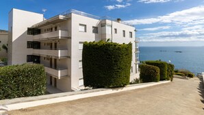 A modern multi-story building with balconies, a clear view of the sea, and a well-maintained garden area. - 3-Bedroom Apartment in Roses with Wi-Fi and Parking (Roses)