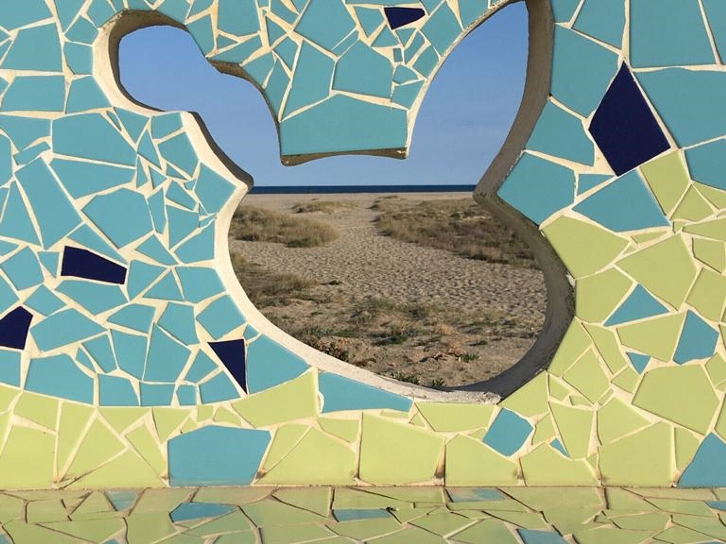 Un mur en mosaïque orné d’une ouverture circulaire dévoilant un paysage désertique.