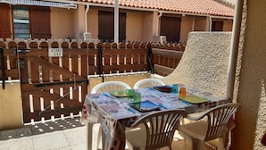Een overdekt terras met een tafel voor twee personen, omringd door een houten hek.