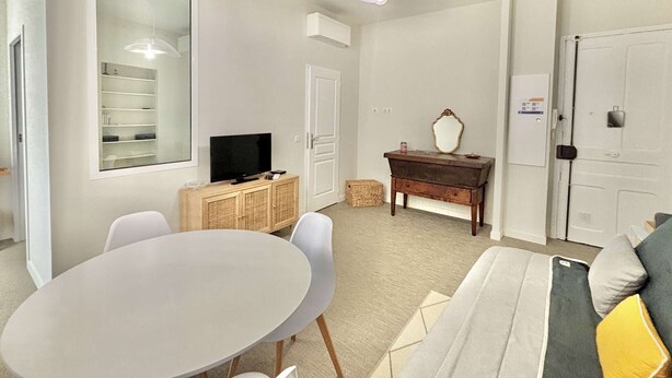 A modern living room with a round table, a sofa, a television, a cabinet, and a mirror.