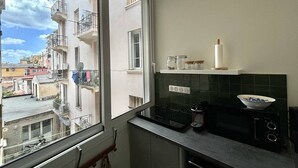 A kitchen with a large window, a stove, a microwave, and a small shelf with jars.