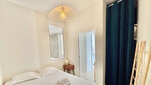 A hotel room with a bed, a mirror, a small table, a door, and a curtain.