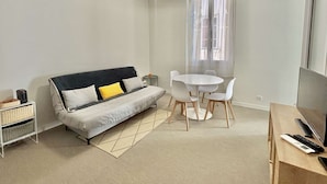 A modern living room with a sofa, a dining table with chairs, a small side table, and a TV stand.