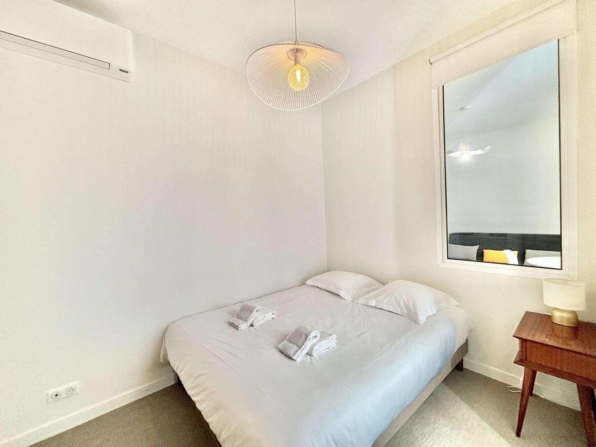 Een slaapkamer met een enkel bed, een nachtkastje met een lamp, een grote spiegel en een plafondlamp.