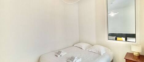 Een slaapkamer met een enkel bed, een nachtkastje met een lamp, een grote spiegel en een plafondlamp.