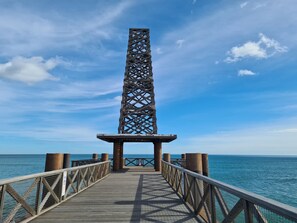 Un muelle de madera que lleva a una estructura metálica con una vista despejada del océano.