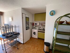 A compact kitchen with a washing machine, microwave, and a small dining area with a metal table and chairs.