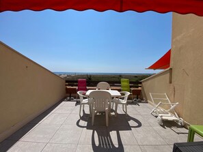 Een balkon met uitzicht op het strand, met een tafel, stoelen, een rode zonnescherm en een groene stoel.