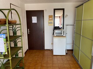 Une cuisine compacte équipée d’un four à micro-ondes, d’un petit réfrigérateur et d’une étagère métallique verte.