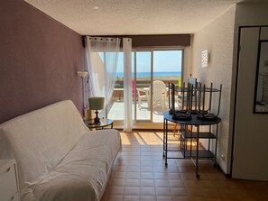 A room with a bed, a table with chairs, a view of the beach, and a balcony door. - Studio Cabin 4 Pers. Sea Front with Parking - Port Leucate (Port Leucate)