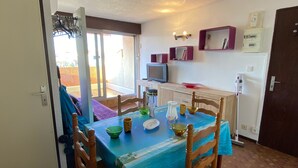 A dining area with a table set for four, chairs, a television, and a window with a view. - Charming T2 Cabin, 4 Guests, Near Beach, Terrace, Parking (Port Leucate)