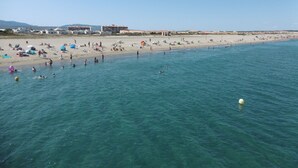 Une plage où l’on voit des gens nager et bronzer, des bâtiments en arrière-plan et un ciel dégagé.