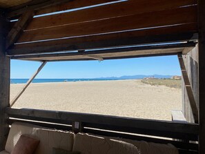Vista da praia a partir de uma cabana de madeira, com um sofá e janela com vista para a areia e o mar.