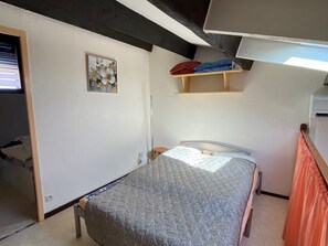 Une chambre à coucher avec un lit, une petite étagère, un tableau et une fenêtre.