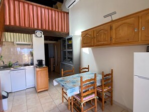 A compact kitchen with a dining area, wooden cabinets, a clock, and a tiled backsplash.