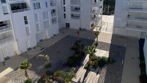 Un immeuble moderne à plusieurs étages, doté de balcons, d’une cour intérieure agrémentée de palmiers et surplombant un ciel dégagé.