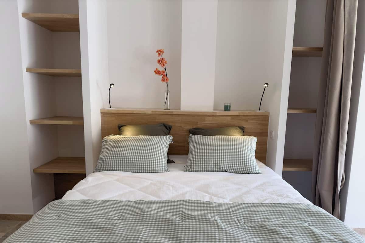 Een net opgemaakt bed met geruit beddengoed, een houten hoofdbord en twee bedlampjes.