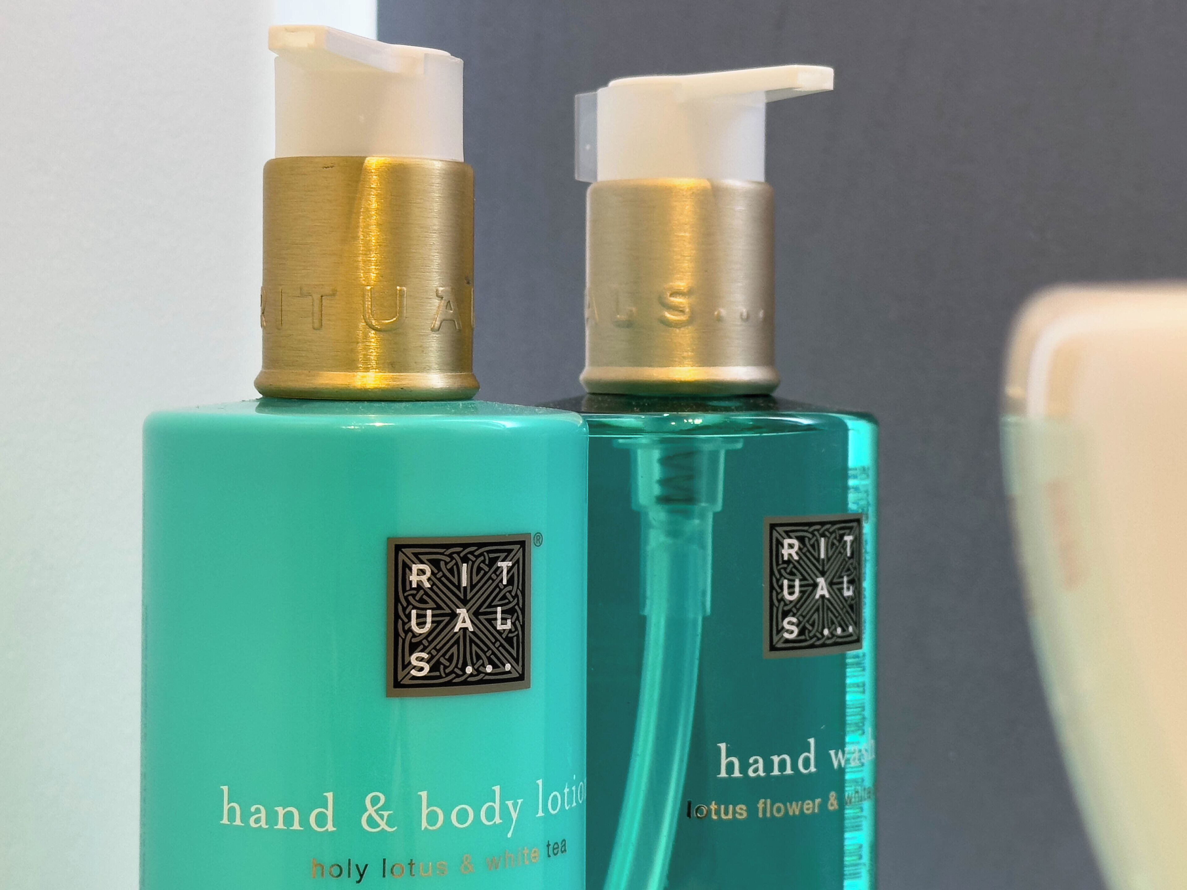 To flasker hånd- og bodylotion med pumpe, mærket 'RITUALS' og 'hand & body lotion holy lotus & white tea'.