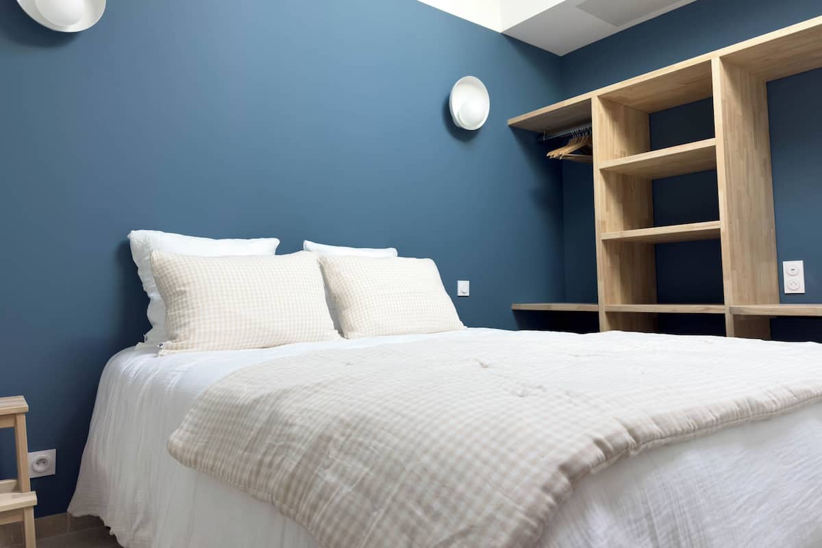 Een slaapkamer met een bed, twee kussens, een nachtkastje, een wandlamp en een inbouwkast van hout.