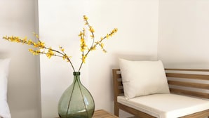 A wooden table with a green vase containing yellow flowers, a magazine, and a wooden bench with a white cushion. - Les Suites du 13 (Aigues-Mortes)