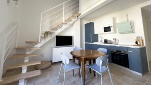 A modern kitchen with a dining area, a staircase, and a flat-screen TV. - Les Suites du 13 (Aigues-Mortes)