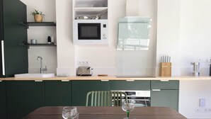 A modern kitchen with a wooden countertop, built-in appliances, and a dining area with a table set for two. - Les Suites du 13 (Aigues-Mortes)