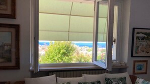 Quarto com janela para uma paisagem verde e o mar.