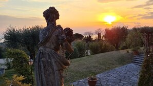 Uma estátua em um jardim com o pôr do sol ao fundo.