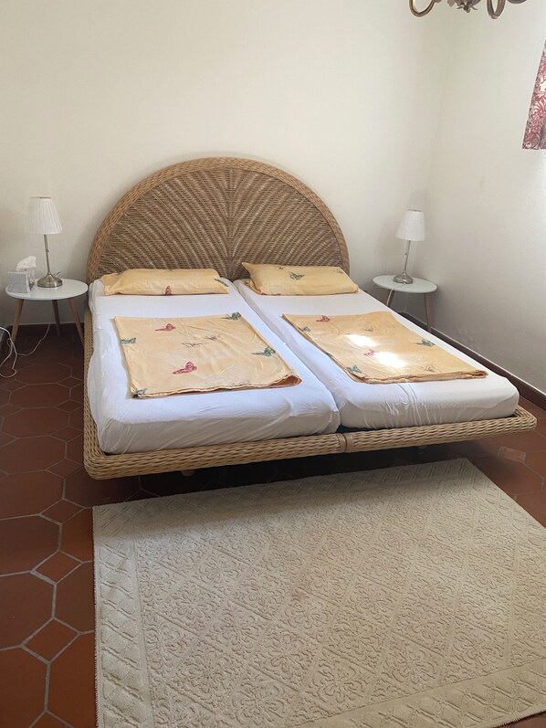 A double bed with a woven headboard, two bedside tables with lamps, and a patterned rug on a tiled floor.