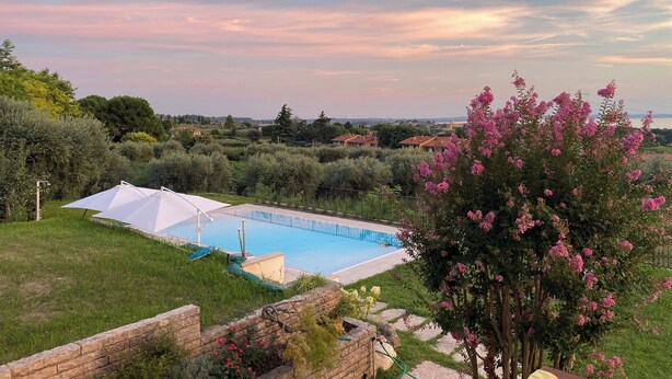Piscina com toldo branco, rodeada por vegetação exuberante e vista para casas ao longe.