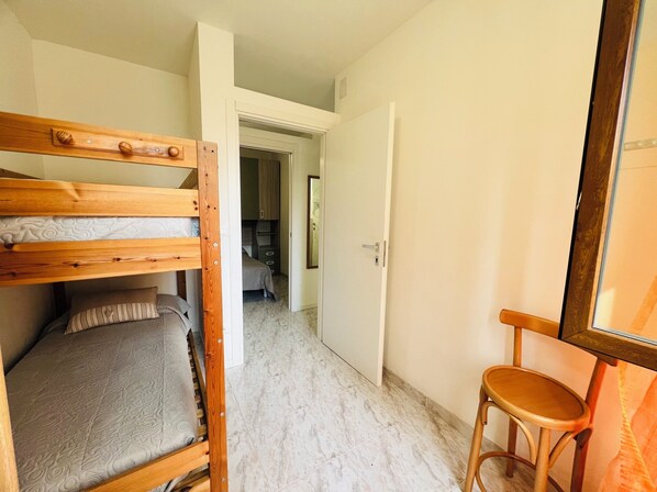 A room with a bunk bed, a small stool, and a door leading to another room.