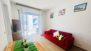 A living room with a red sofa, a wooden table with magazines, a potted plant, and a balcony with a view. - Relaxing apartment near the beach (Bibione)
