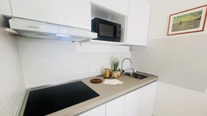 A modern kitchen with white cabinetry, a black induction cooktop, a microwave, and a stainless steel sink. - Relaxing apartment near the beach (Bibione)