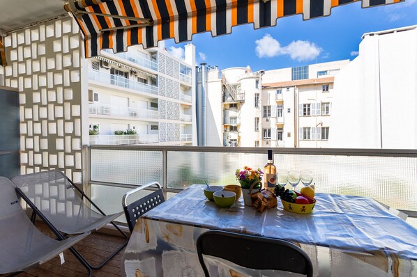 Varanda com mesa posta para dois, incluindo toalha de mesa, tigelas, cesta de frutas e uma garrafa.