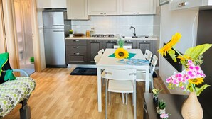 Une cuisine compacte équipée d’un réfrigérateur, d’une cuisinière et d’un évier. On y trouve une table à manger avec des chaises et un vase rempli de fleurs.