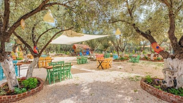 An outdoor seating area with tables and chairs, surrounded by trees and plants.