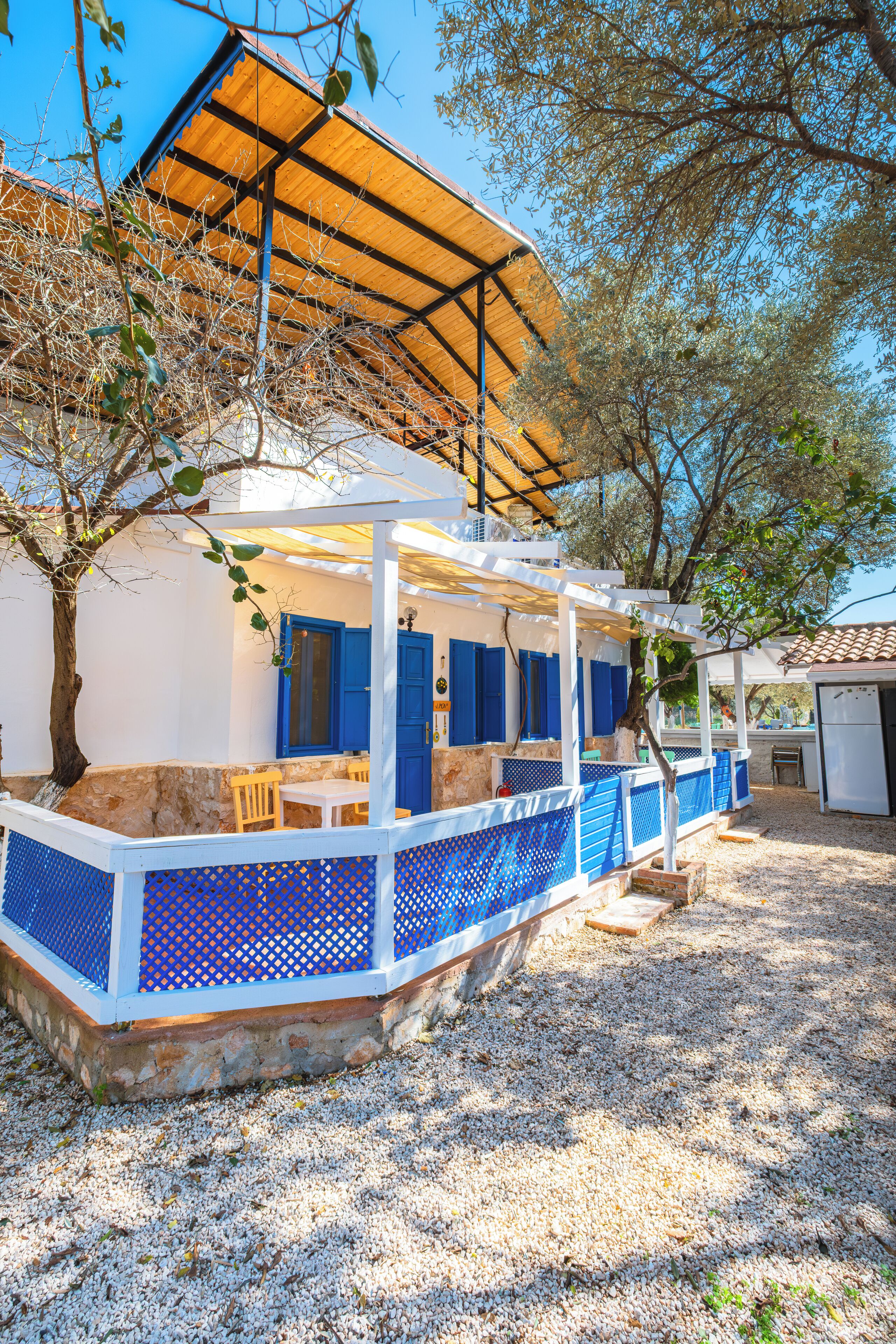 A covered outdoor seating area with a stone wall, blue shutters, and a wooden pergola.