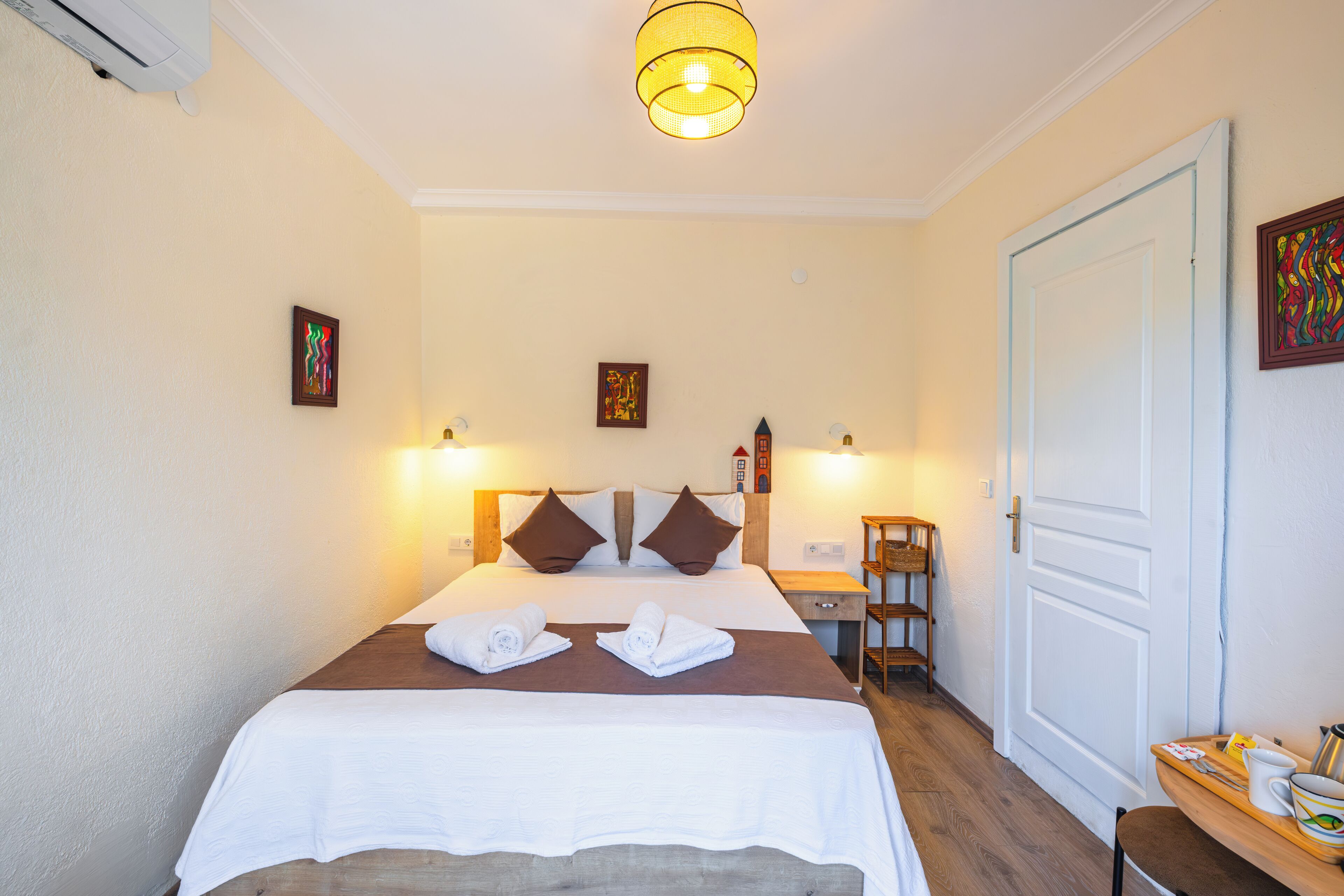 Una habitación de hotel con una cama, dos lámparas de pared, una mesita de noche de madera, una silla y una puerta.