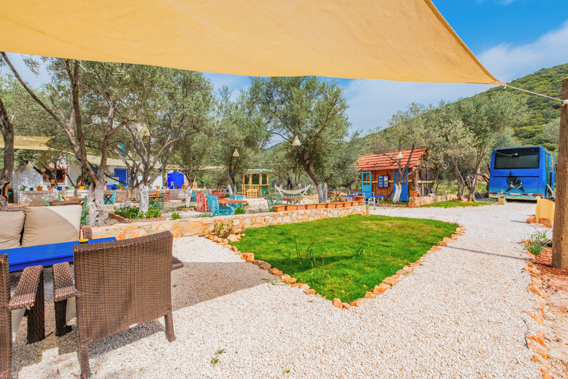 Un patio con mesas al aire libre, un pequeño jardín y un autobús azul estacionado cerca.