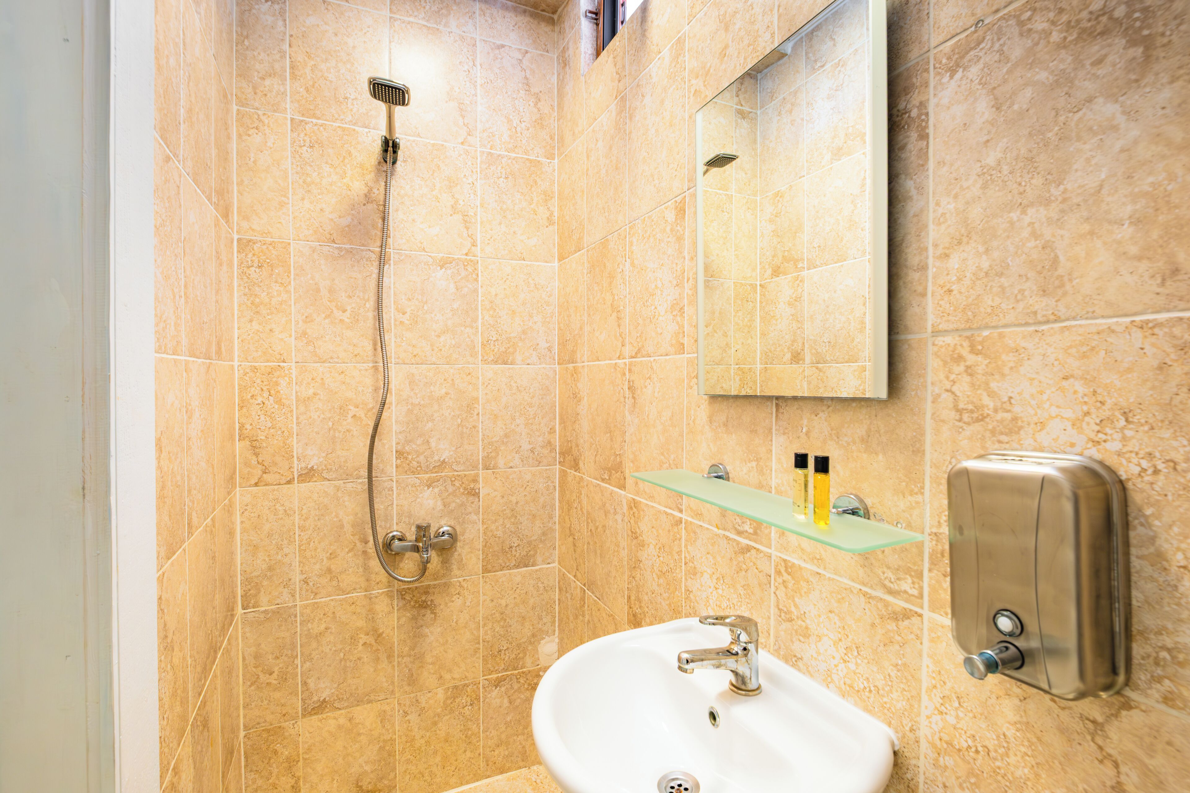 Une salle de bain équipée d’une douche, d’un lavabo, d’un miroir et d’une étagère pour les articles de toilette.