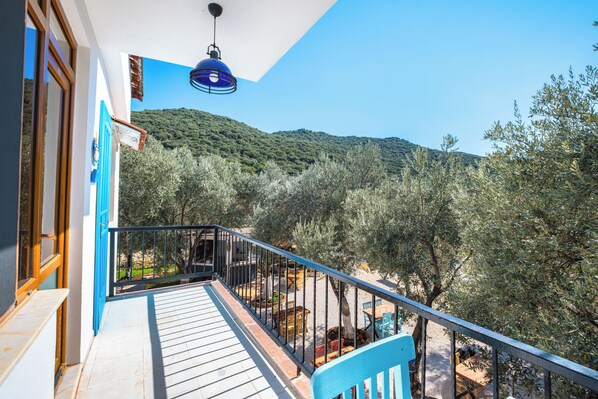 Un balcón con vista a un paisaje montañoso, barandilla azul y mobiliario exterior.