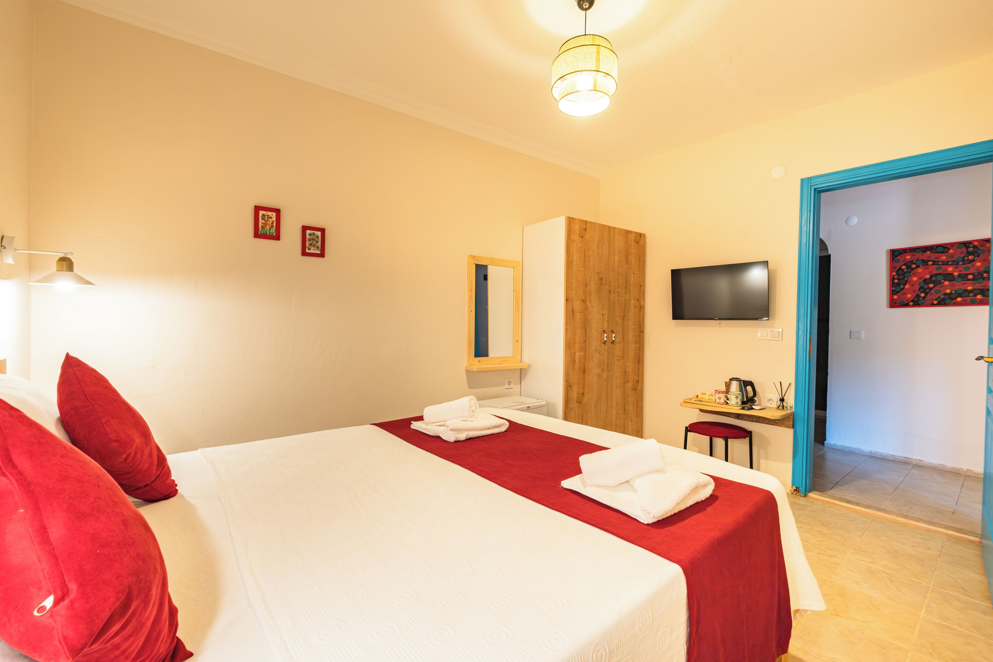 Habitación de hotel con cama, almohadas rojas, armario de madera, televisor y escritorio con silla.