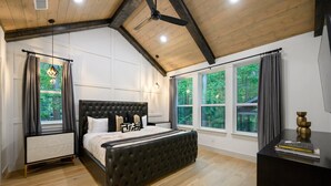 Un dormitorio con una cama grande, una mesita de noche, un aparador y una ventana con cortinas.