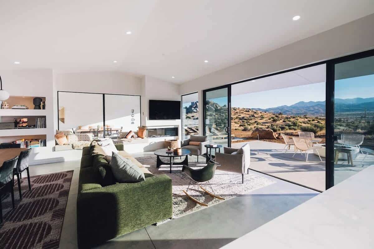 Una sala de estar moderna con un televisor grande, asientos cómodos y vistas a un paisaje desértico a través de amplios ventanales.