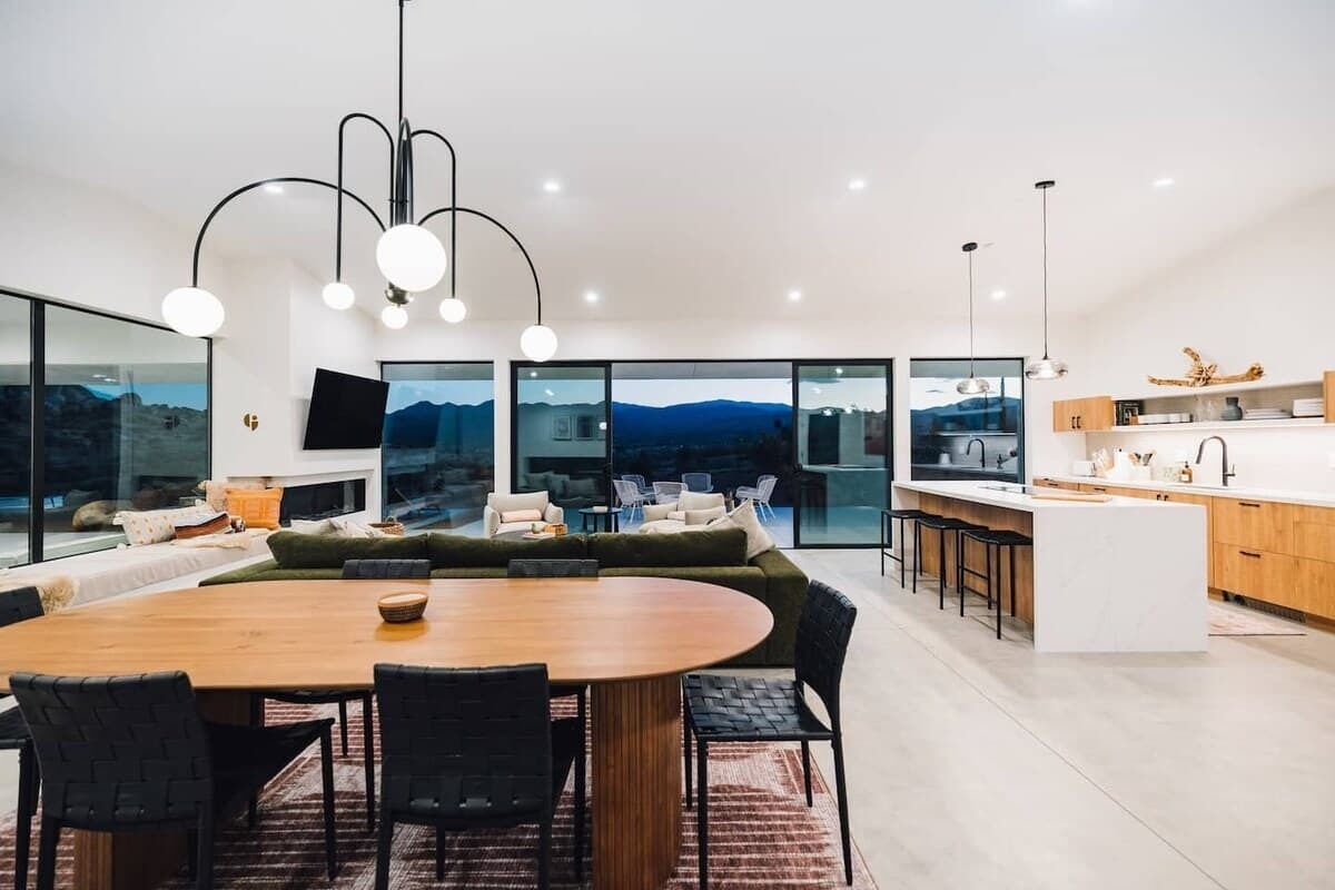 A modern kitchen with a central island, a dining area with a round table, and a large window offering a mountain view.