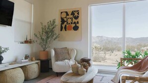 Uma sala de estar moderna com uma janela grande, um sofá branco, uma mesa de centro e um vaso com planta.
