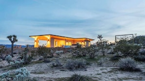 Uma casa moderna com telhado plano e janelas amplas, rodeada por vegetação do deserto.
